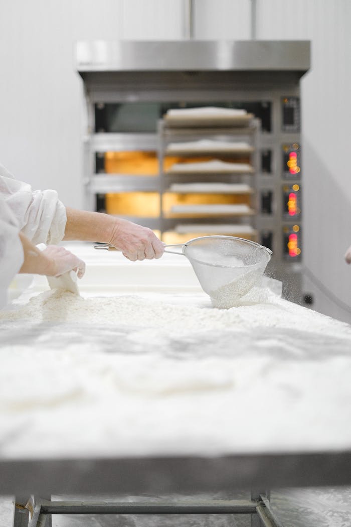 Close-up of hands sifting flour in a bakery, highlighting the industrial baking process.