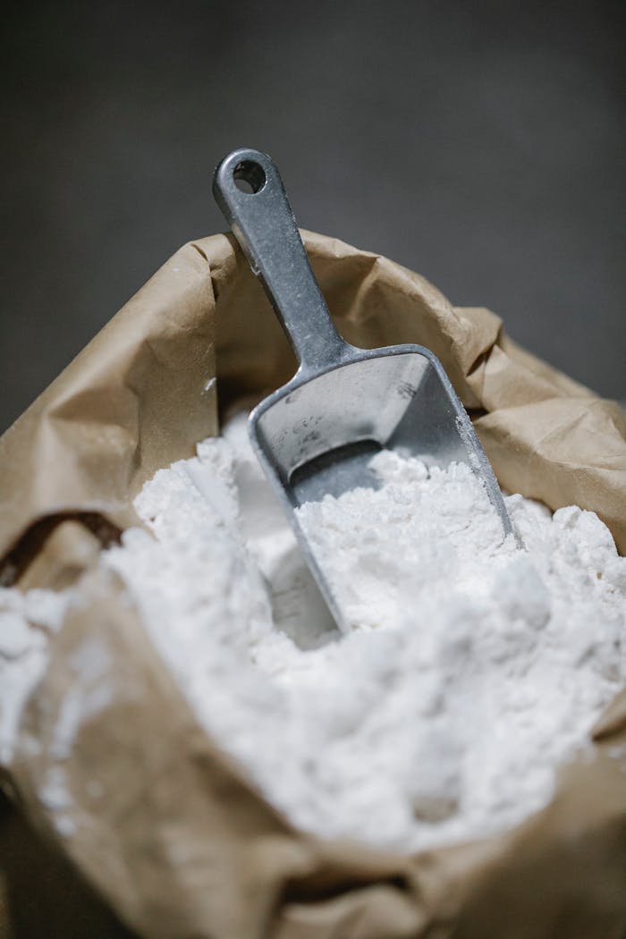 A metal scoop in a bag of flour creates a rustic culinary scene perfect for baking themes.